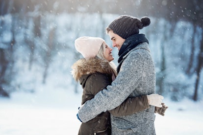 A couple smiles and hugs each other while the snow falls outside.