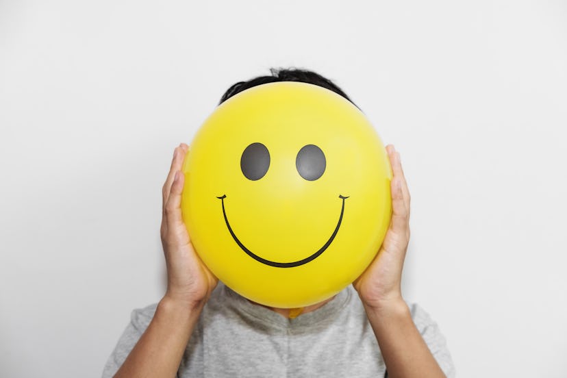 A man holding yellow balloon with smile face emotion instead of head. Positive Thinking concepts. hi...