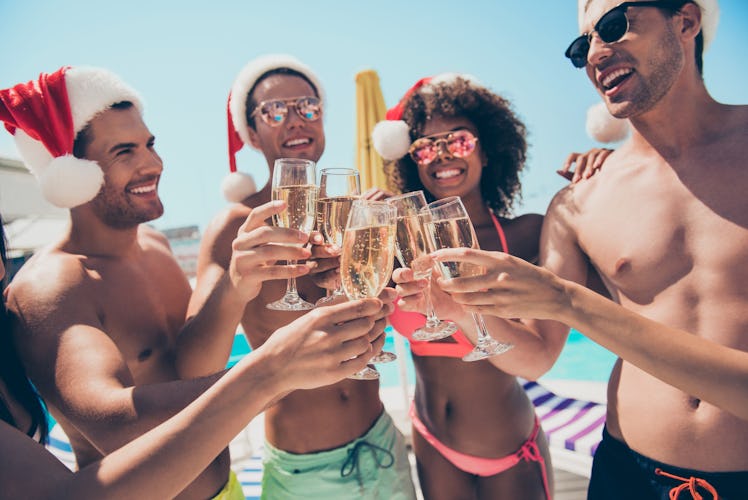 A group of friends dressed in bathing suits and Santa hats smile and toast their champagne flutes on...