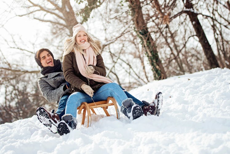 A man and woman laughing in snow on sled, thanks to some snow puns.