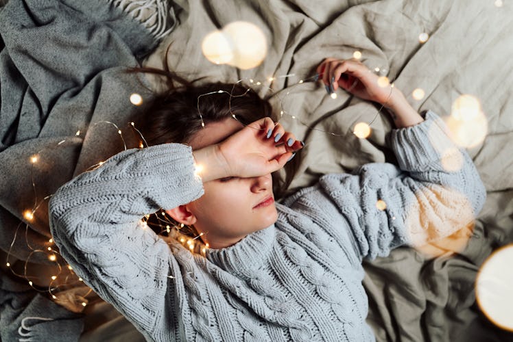 Young white woman lying in bed with fairy Christmas lights and bokeh around, shallow selective focus