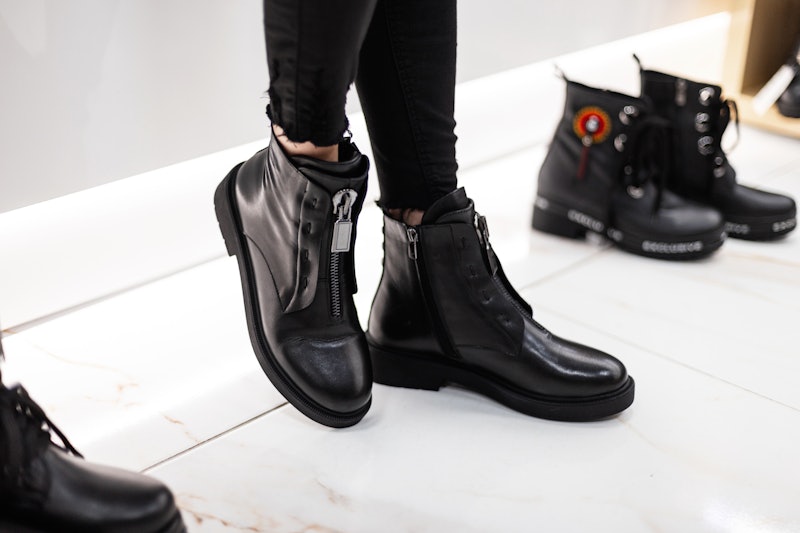 Young fashion woman in black stylish jeans in fashionable leather  boots stands on the white tile in...