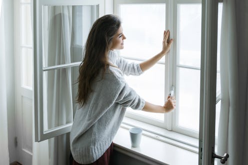 Woman is opening window to look at beautiful snowy landscape outside