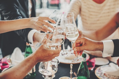 Hands toasting with champagne glasses at wedding reception outdoors in the evening. Family and frien...