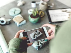 A woman takes a picture of her holiday gift on her phone after wrapping it in green and white paper.