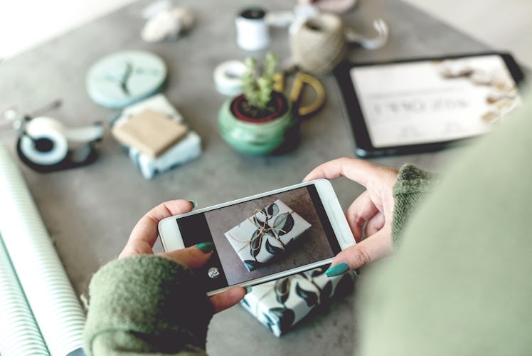 A woman takes a picture of her holiday gift on her phone after wrapping it in green and white paper.