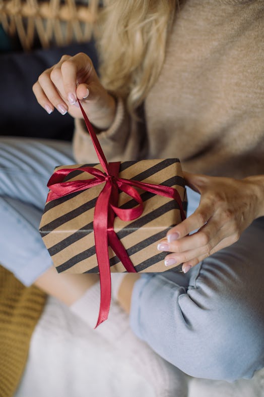 A blonde woman opens up a holiday gift with a red ribbon on Christmas.