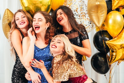Friends wearing sparkly dresses pose with balloons at a birthday party.