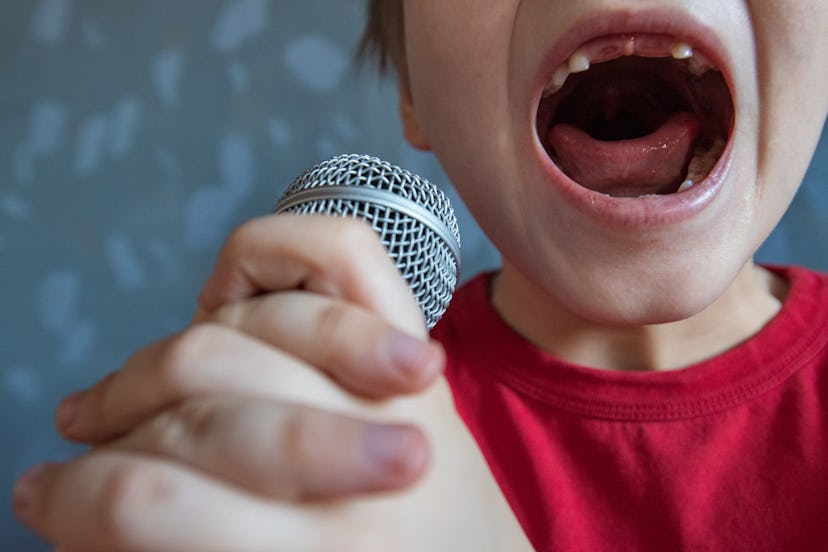 charming kid sings into microphone and opens her mouth wide with milk teeth dropped out.