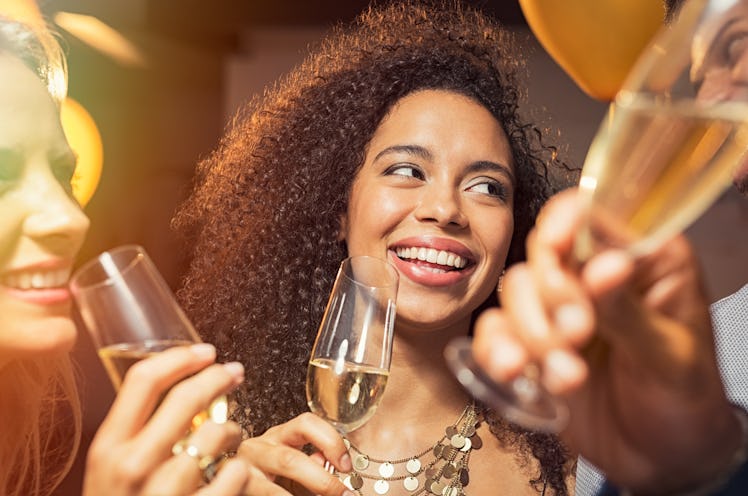 Happy young african woman holding wine glass with friends at party. Portrait of beautiful black girl...