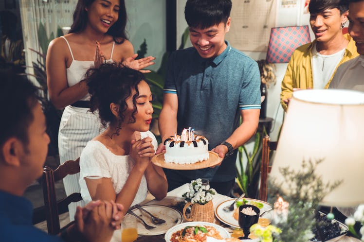 Friends celebrate a birthday at a dinner table while the birthday girl blows out the candles.