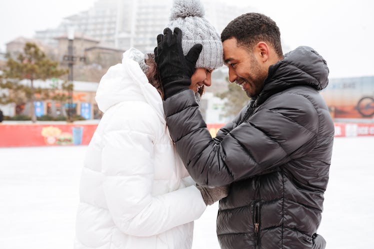 Photo of young happy loving couple skating at ice rink outdoors. Looking each other.