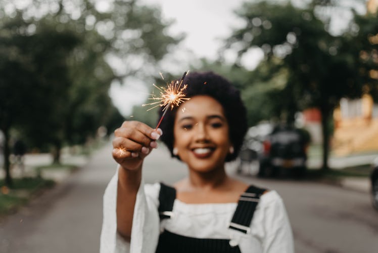 A woman holds a sparkler while posing for a camera on New Year's Eve.