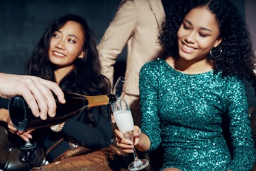 Two girls sit on a couch on New Year's Eve holding their champagne glasses.