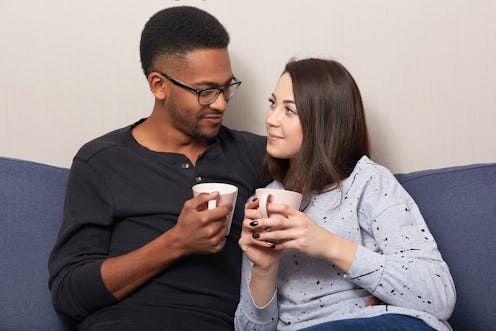 Horizontal shot of lovely multiethnic girlfriend and boyfriend drink coffee or tea together, pose at...