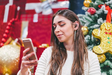 Young smiling attractive girl sitting near christmas background, having video conference with her fr...
