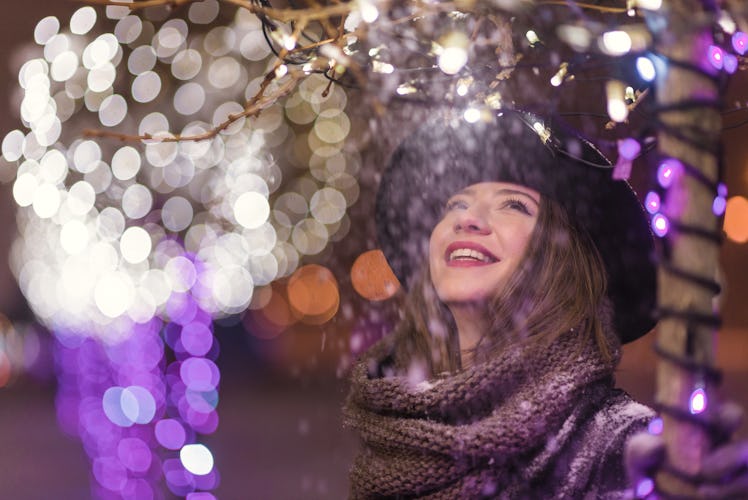 Young girl standing in front of Christmas tree lights at night with snowflakes falling, snowing