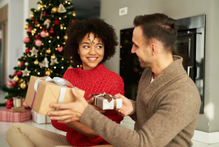 A couple smiles and shares Christmas gifts in their living room over the holidays. 