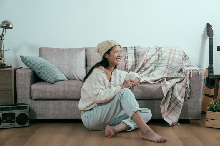 A fashionable woman drinks coffee near a couch in a cabin while on a winter vacation.