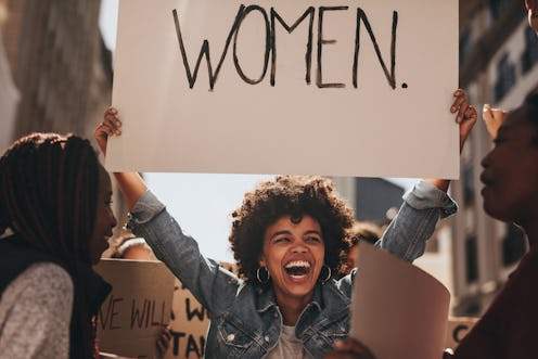 Laughing young woman holding a banner during a protest. Group of females activist protesting on road...