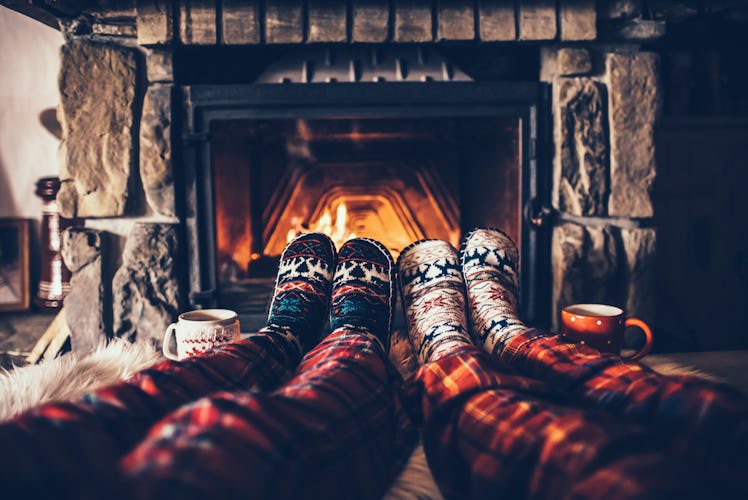 Two people wearing flannel PJs and cozy socks sit next to the fireplace in a bed and breakfast over ...