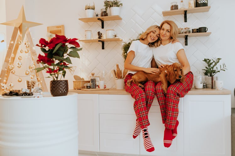 A mother and daughter sit in holiday pajamas with their dog on their kitchen counter.