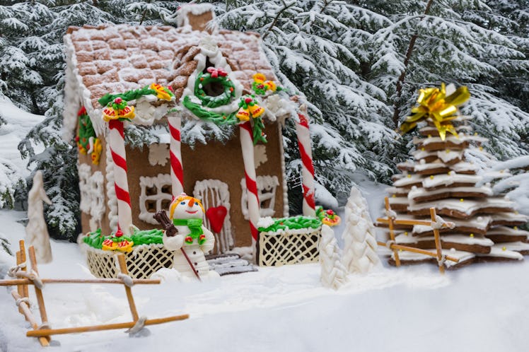 Snow-covered homemade gingerbread house, gingerbread Christmas tree and a sugar mastic snowman on fo...