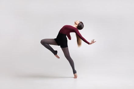 young beautiful woman dancer with long brown hair wearing maroon swimsuit posing on a light grey stu...