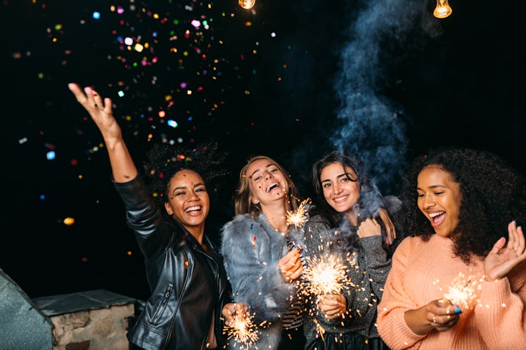 A group of friends celebrate New Year's Eve outside with sparklers and confetti.