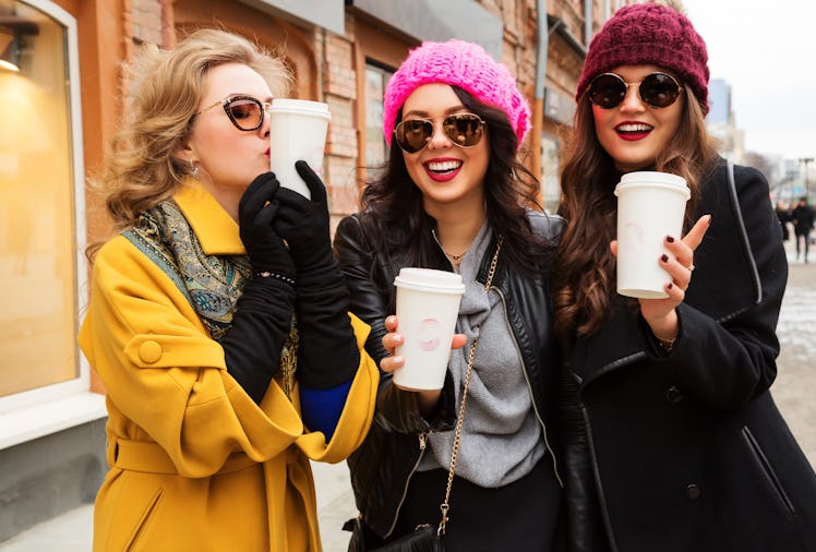 Outdoors fashion portrait of three young beautiful women friends drinking coffee. Smiling and going ...