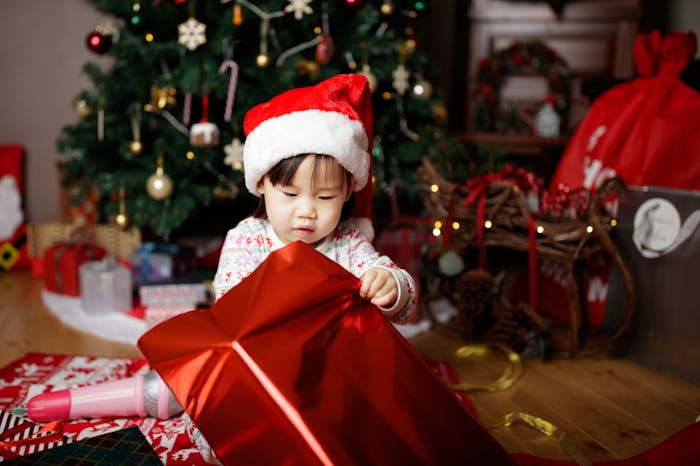 toddler baby girl wearing santa claus costume opening gift box in front of christmas tree