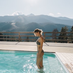 Young woman spending winter or spring vacation in luxury spa resort with swimming pool over alpine m...