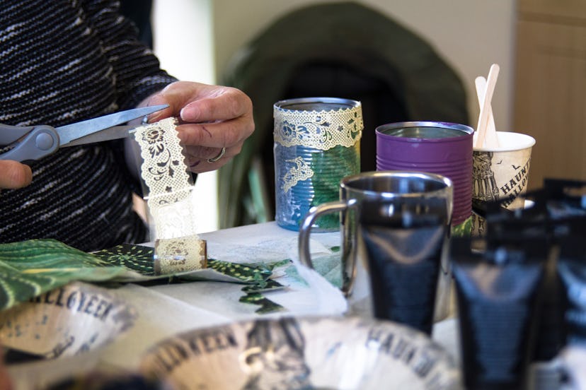 Recycling tin cans into decorated plant pots. Person cutting lace beside crafting table with craftin...