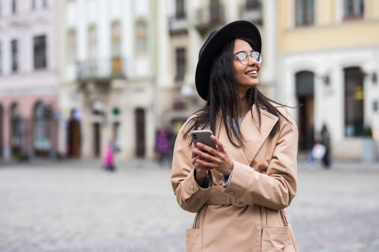Portrait of happy woman in black hat walking and using a phone on a city street