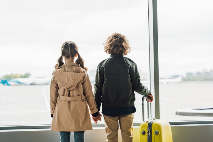 back view of kids holding hands, standing near window in waiting hall in airport