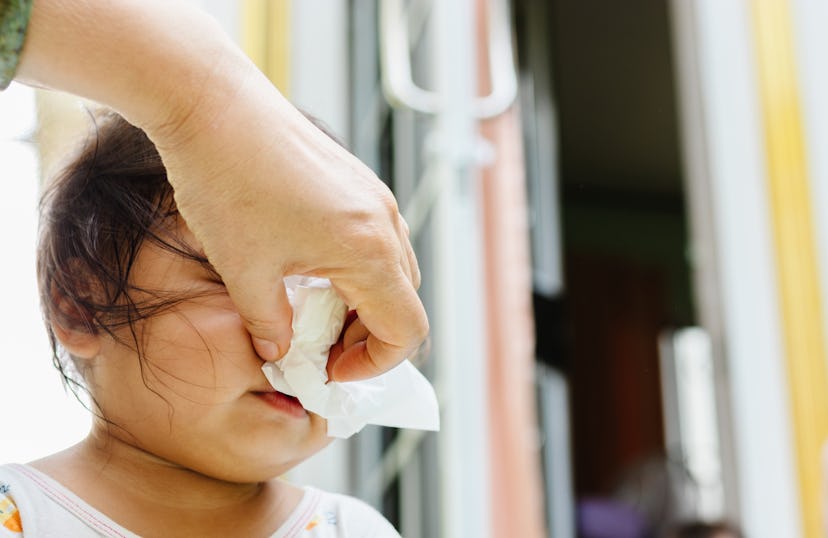 Mother helping to blow baby nose with paper tissue.