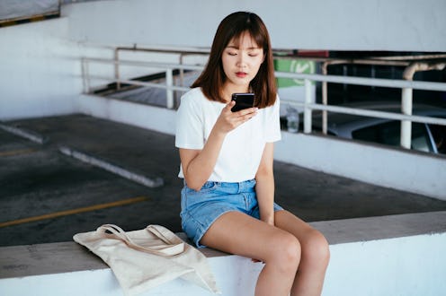 Woman sitting at the parking lot, typing her phone.
