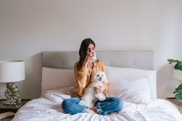 A girl sits and relaxes on her bed with her dog and drinks tea.