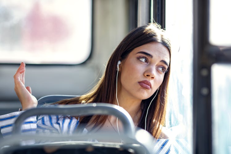 Pensive young woman traveling, holding smart phone and listening music. Sad teenage girl listening t...