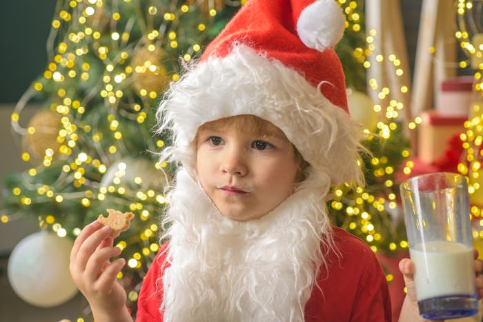 Kid dressed as Santa Claus eating a cookie and holding a glass of milk