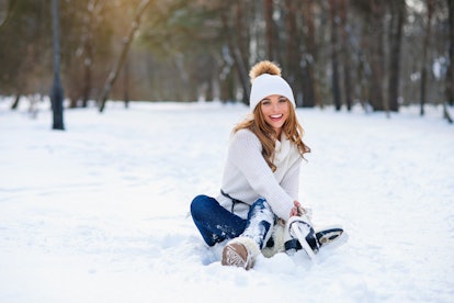 Young woman sits on the frosty snow in winter park. Winter holidays concept.