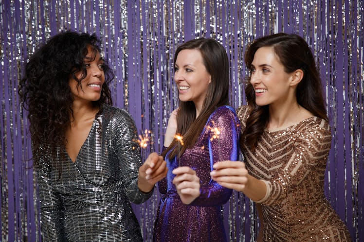 Women in fancy sparkling dresses posing isolated over vibrant purple violet silver background. Posit...