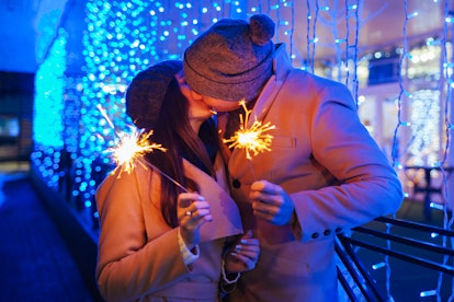 Young loving couple burning sparklers by holiday illumination. Christmas and New year concept