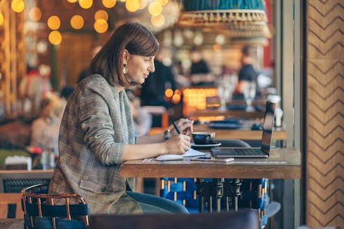 Young woman in blazer with laptop in the cafe near the window. Professions is a blogger, freelance...