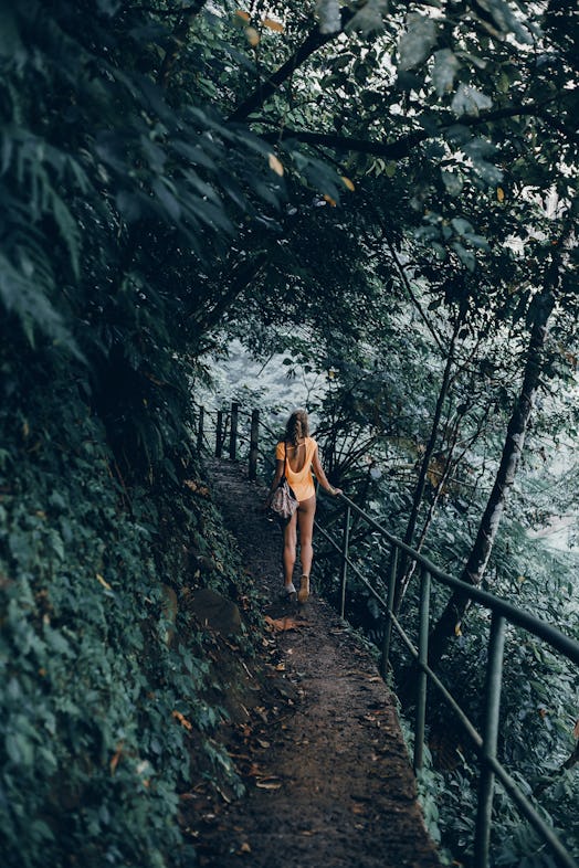 A woman walks down a hiking trail in a tropical forest while on vacation.