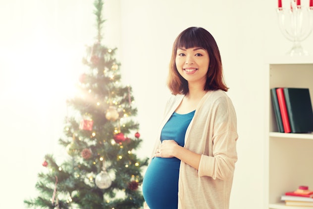pregnancy, winter holidays and people concept - happy asian pregnant woman at christmas tree at home