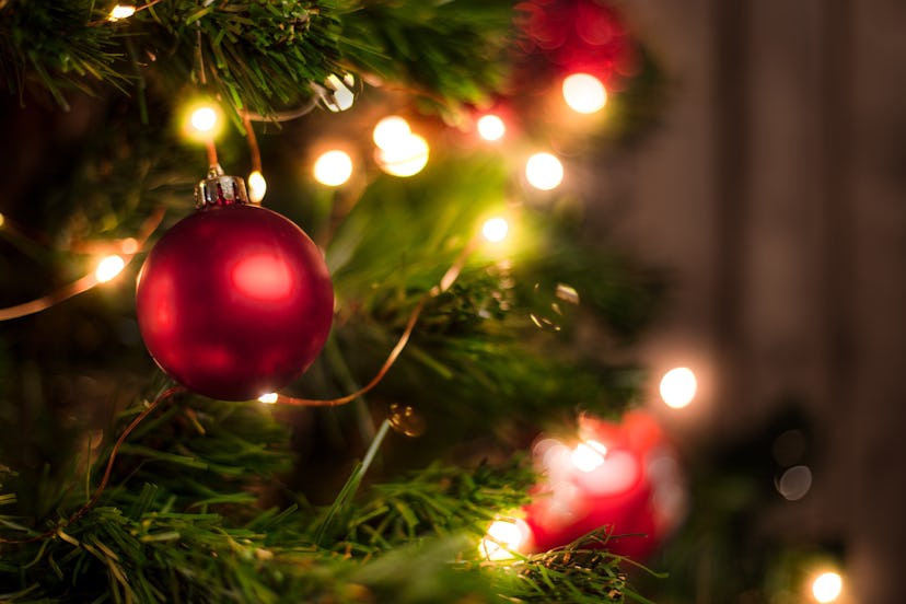 Red Christmas ball on a Christmas tree in an article about can you leave your christmas lights on ov...