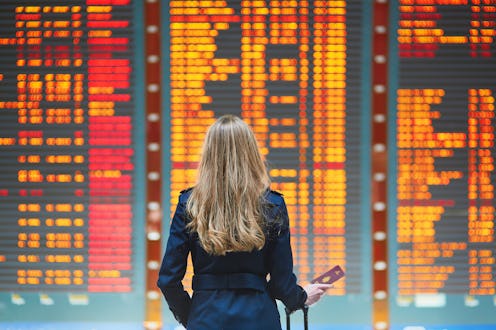 Young woman in international airport looking at the flight information board, checking her flight