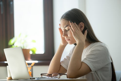 Exhausted young female worker is tired from work. Stress and headache behind laptop on job. Overwork...