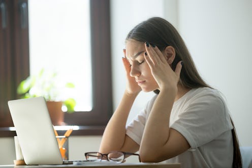 Exhausted young female worker is tired from work. Stress and headache behind laptop on job. Overwork...